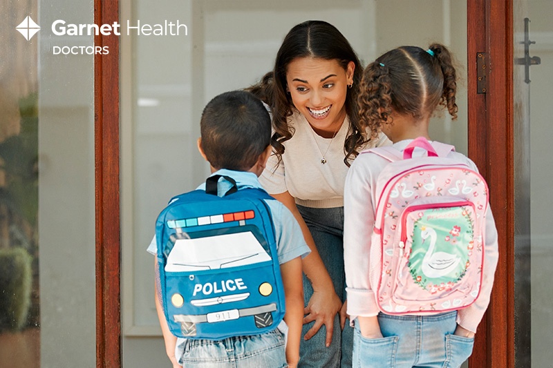 Mother saying goodbye to children wearing backpacks